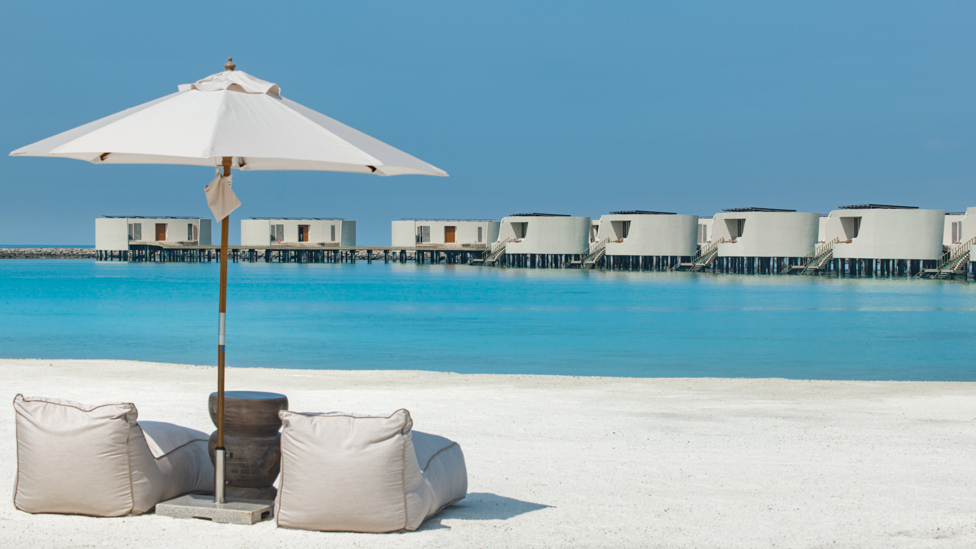 A snapshot of the private beach including a couple sun loungers and a view of the overwater villas