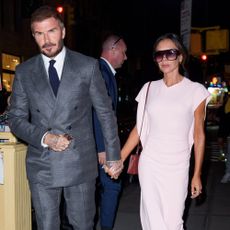 Victoria Beckham hols hands with David Beckham wearing a pink dress, burgundy heels and a burgundy bag.