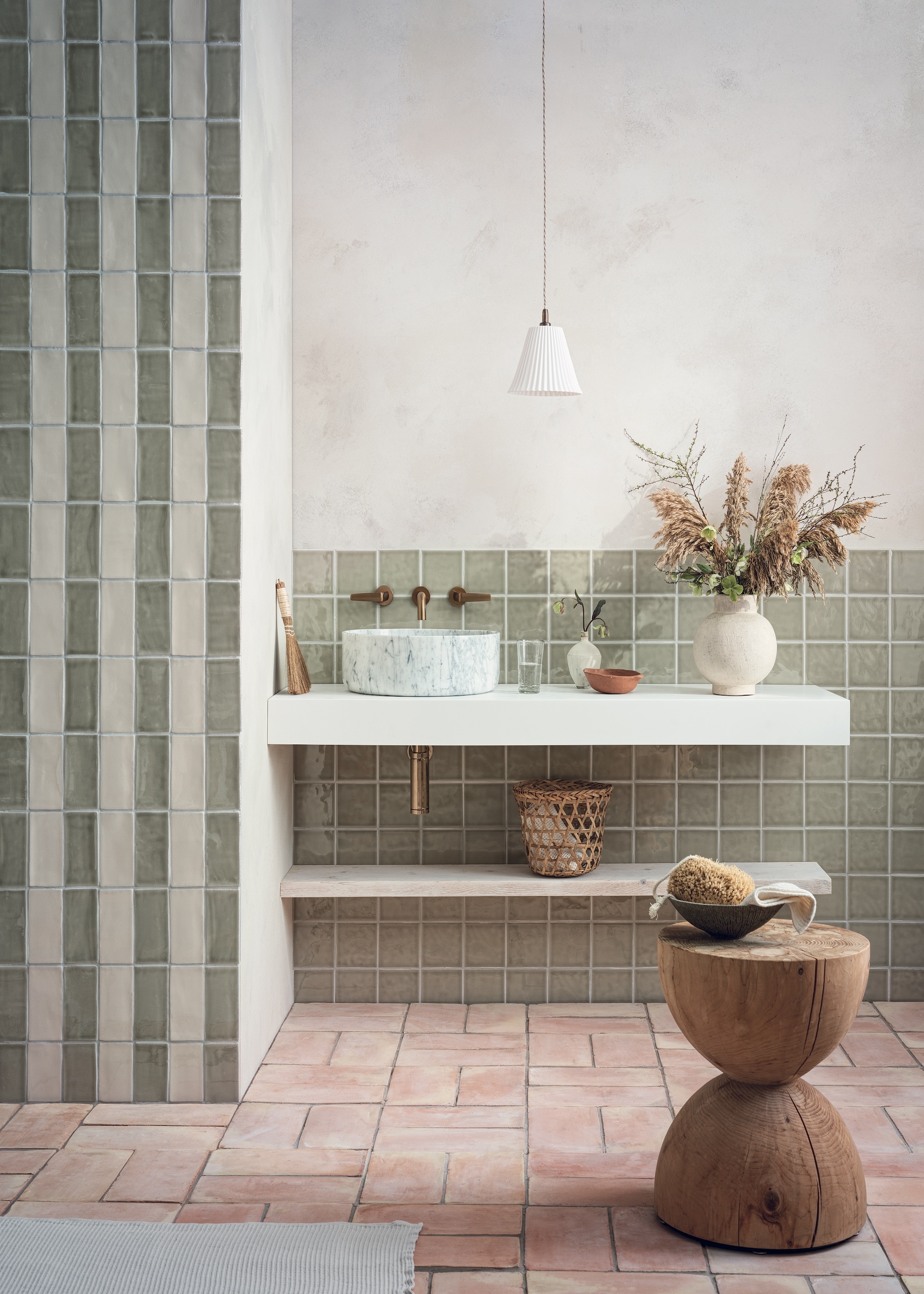 A warm and calm bathroom shown with sage green, off white and terracotta tiles, natural wood accessories and brushed brass taps
