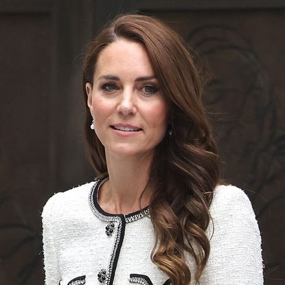 Kate Middleton has long brown hair and is wearing a white tweed jacket with black detailing