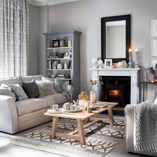 Grey living room with light colored sofas, woodburning stove and geometric rug