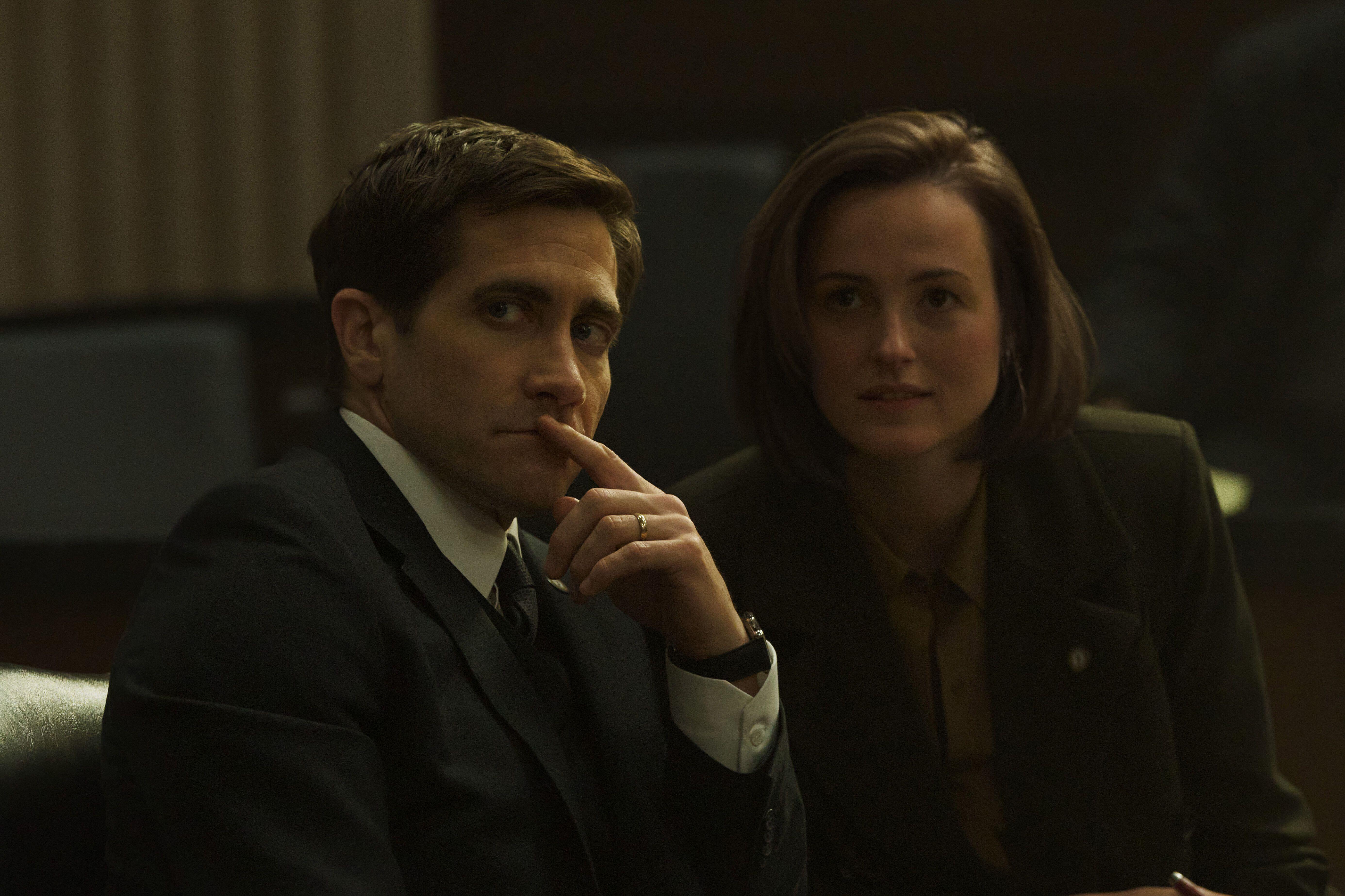 jake gyllenhaal wears a suit and sits in a court room with a woman in a still from presumed innocent