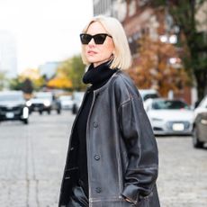 Naomi Watts wearing a turtle neck under a leather jacket and black cat eye sunglasses