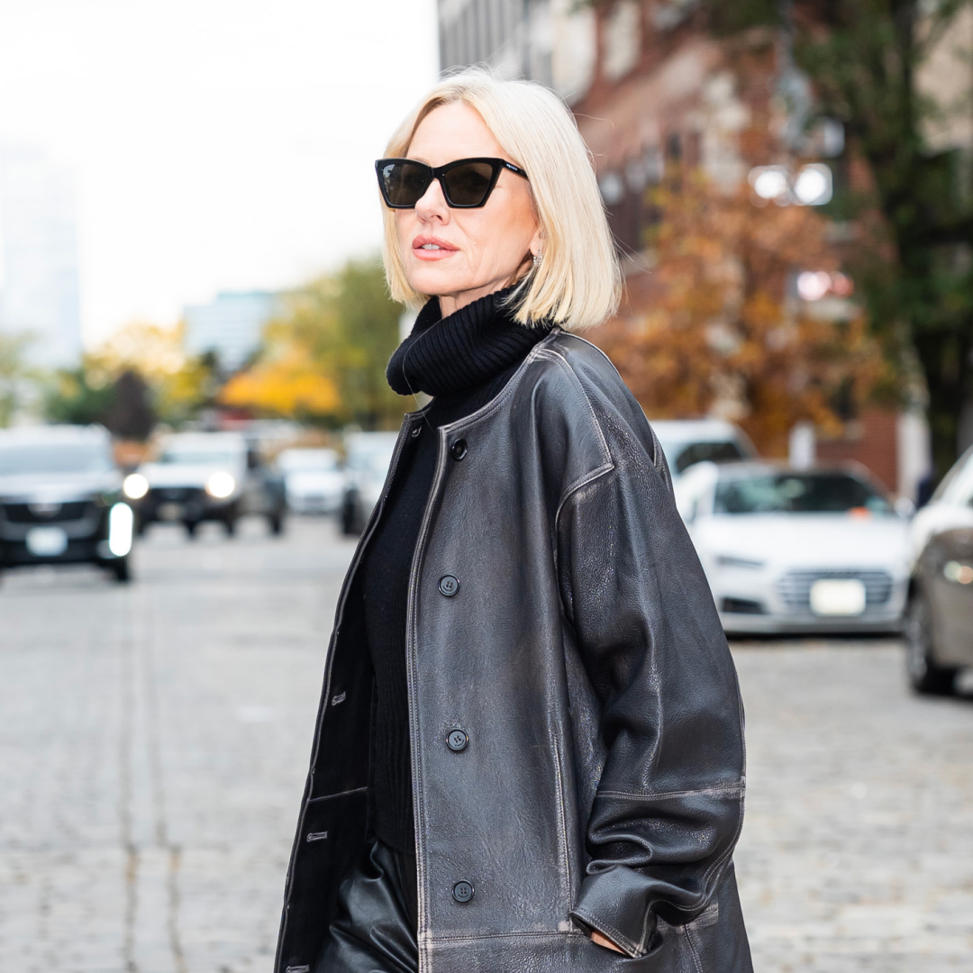Naomi Watts wearing a turtle neck under a leather jacket and black cat eye sunglasses