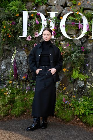 Lily Collins at the Dior Cruise 2025 Show held at Drummond Castle on June 3, 2024 in Perthshire, Scotland dressed in a black wool and silk jacket, black cashmere turtleneck, black wool and silk skirt, and slouchy black boots from the brand