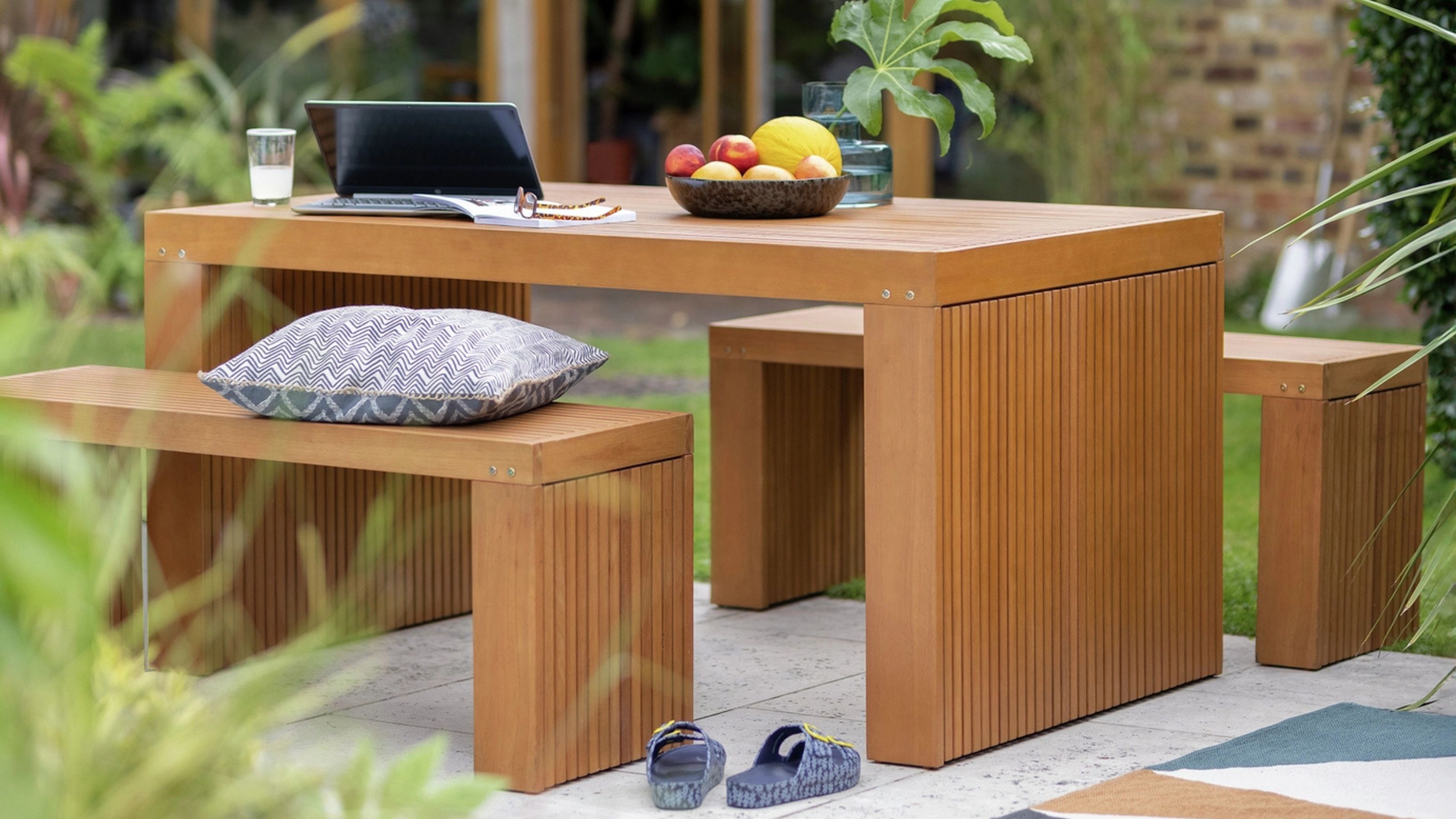 Habitat Samoa 4 Seater Eucalyptus Patio Set in a garden next to an outdoor rug with a laptop and a fruit bowl on top of the table