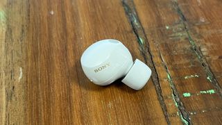 The Sony WF-1000XM5 wireless earbuds in white on textured wooden background