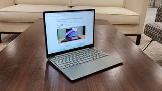 Surface Laptop Go 3 on a brown wooden table with a beige sofa in the background with a 