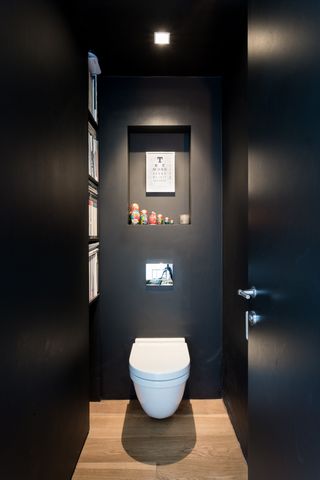 black powder room with alcove above toilet and one on the side with books, wooden floor