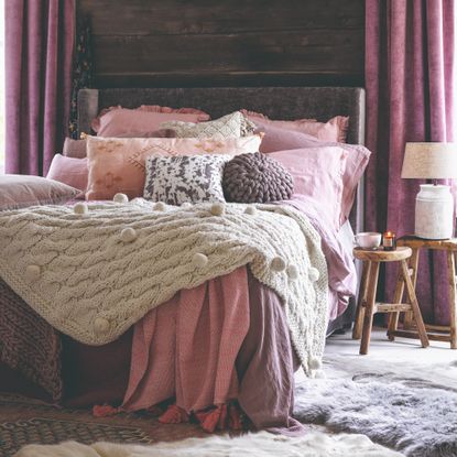 A bedroom with layered bedding on the bed and layered rugs on the floor with the nearest one to the side of the bed being a soft, shaggy style