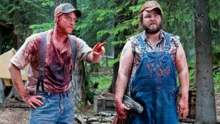 Tucker and Dale covered in blood and holding a disembodied torso in the woods