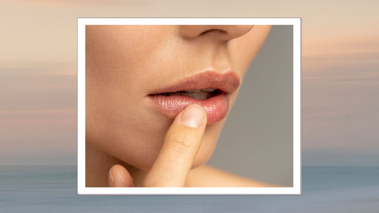 A close up shot of a woman&#039;s mouth, with her finger touching her bottom lip on a graduated backdrop