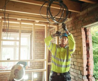 electrician cutting wires for first fix wearing hi vis and hard hat in semi-constructed house