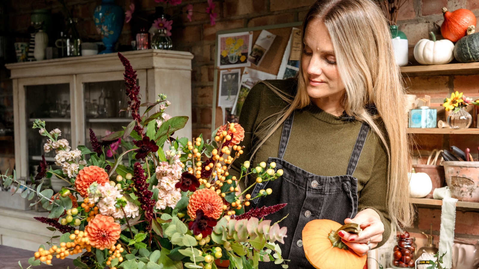 Woman holding pumpkin lid and looking at floral design in a pumpkin