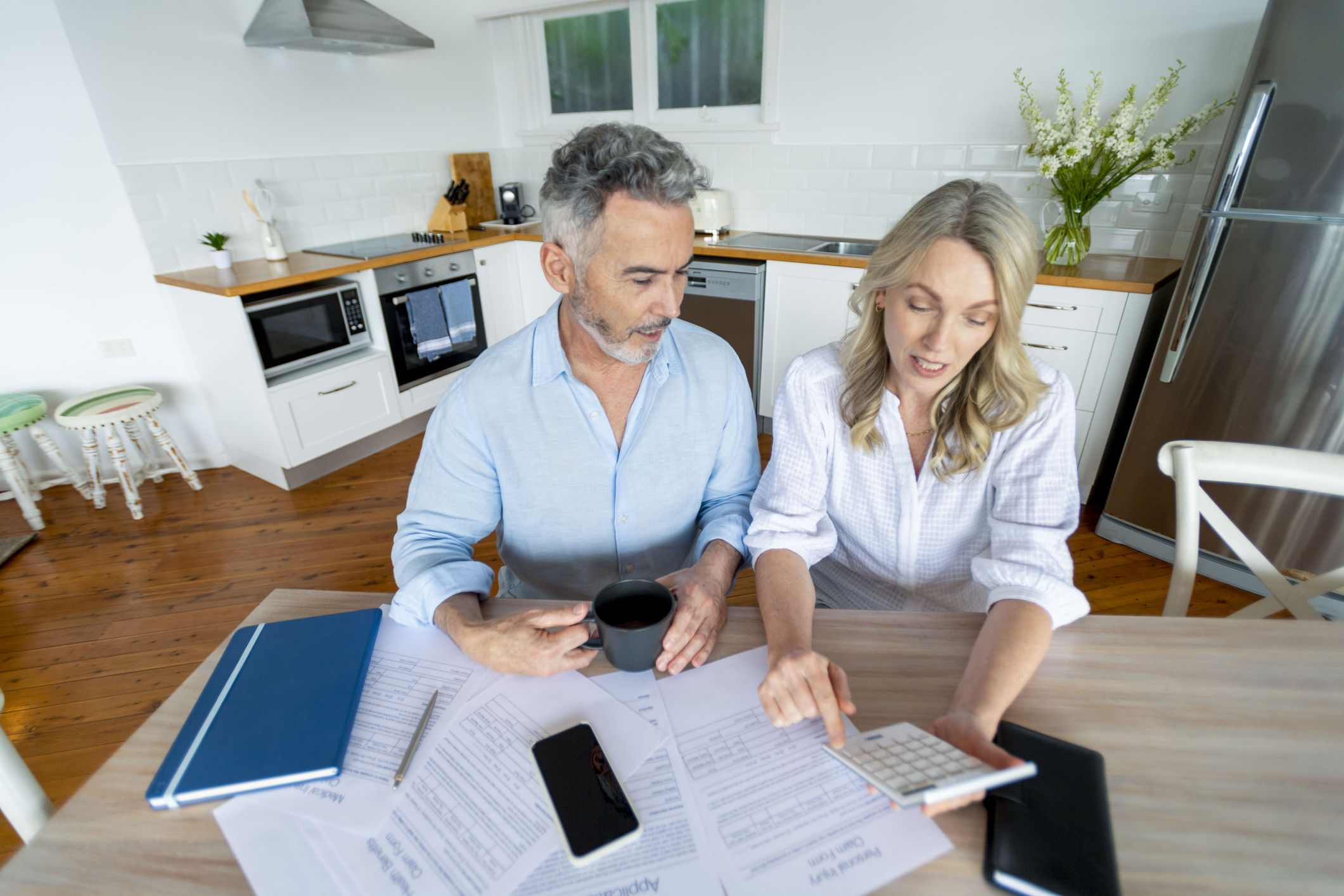 Mature couple doing paperwork and paying bills at home. They are working at the dining room table using a calculator. They look upset. There are medical and mortgage documents on the table.