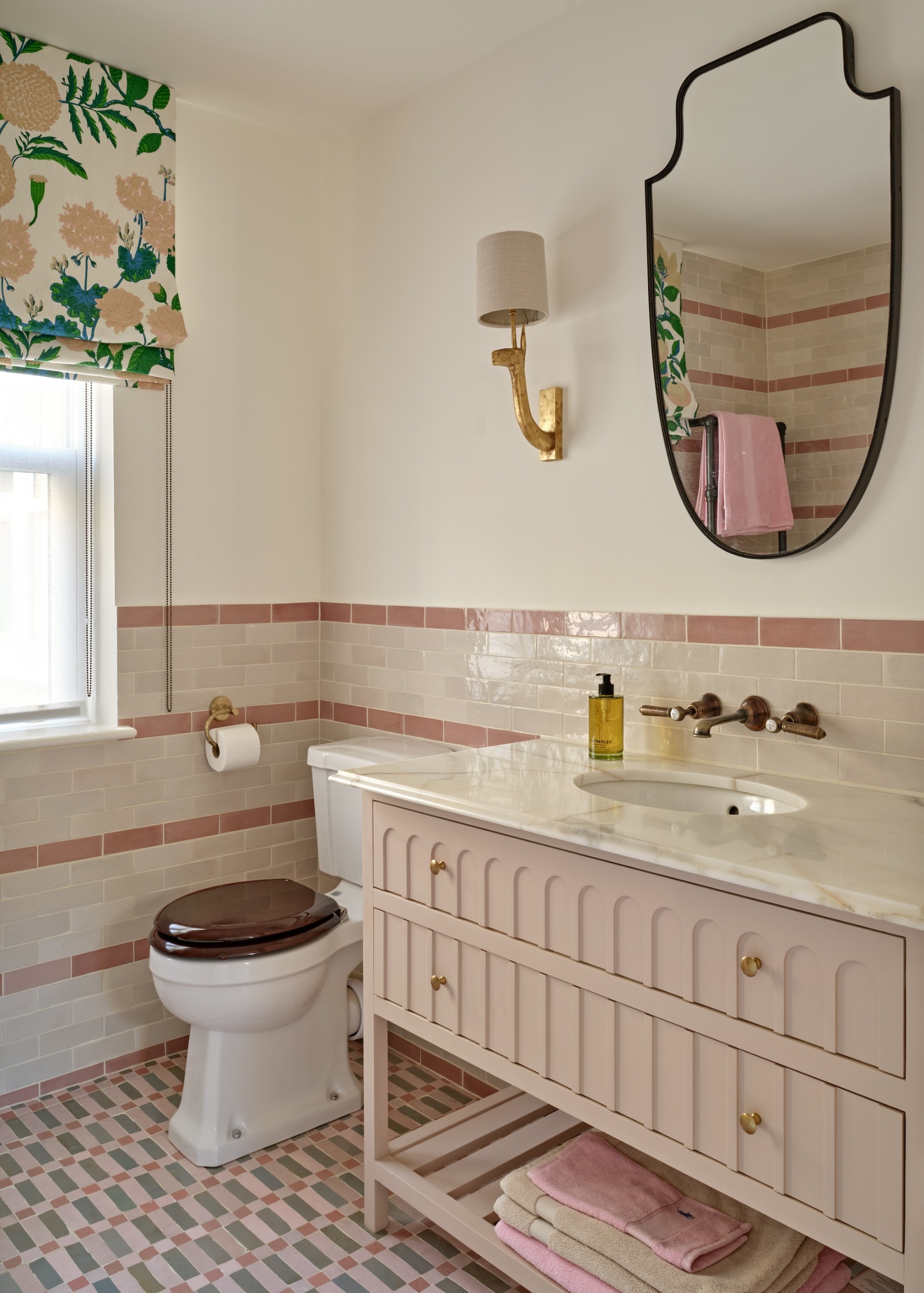 a pretty bathroom with a pale pink vanity unit, patterned tiled flooring and vintage style accessories