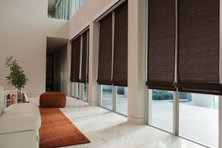 Dark bamboo shades along row of glass sliding doors in modern home with orange pouffe seat