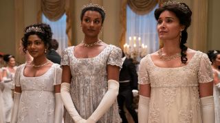 (L to R) Charithra Chandran as Edwina Sharma, Simone Ashley as Kate Sharma, Shelley Conn as Mary Sharma all wearing white and looking forward.