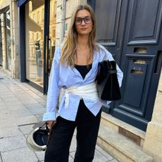Influencer @annelauremais wears black leather ballet flats with a blue shirt, black trousers and white scarf tied around her waist.