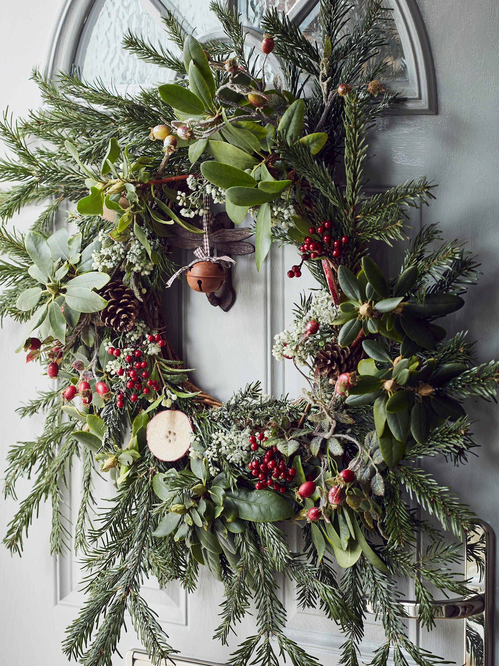 Close up of a festive wreath containing foliage, berries and rose hips, on a grey front door