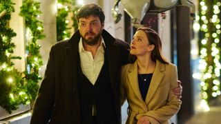 Strike: The Ink Black Heart Cormoran Strike (Tom Burke); Robin Ellacott (Holliday Grainger) walk along with his arm around her.