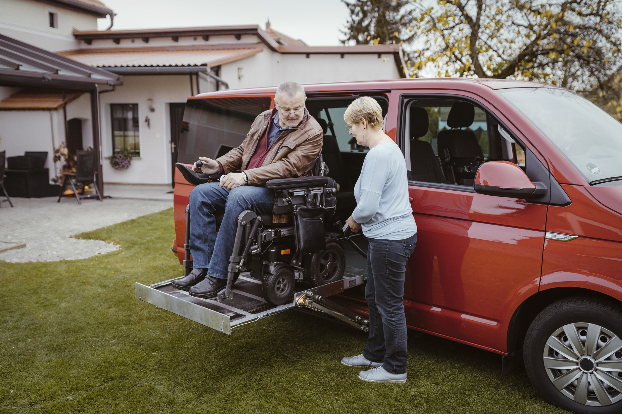 Older man in a wheelchair being helped out of a car.
