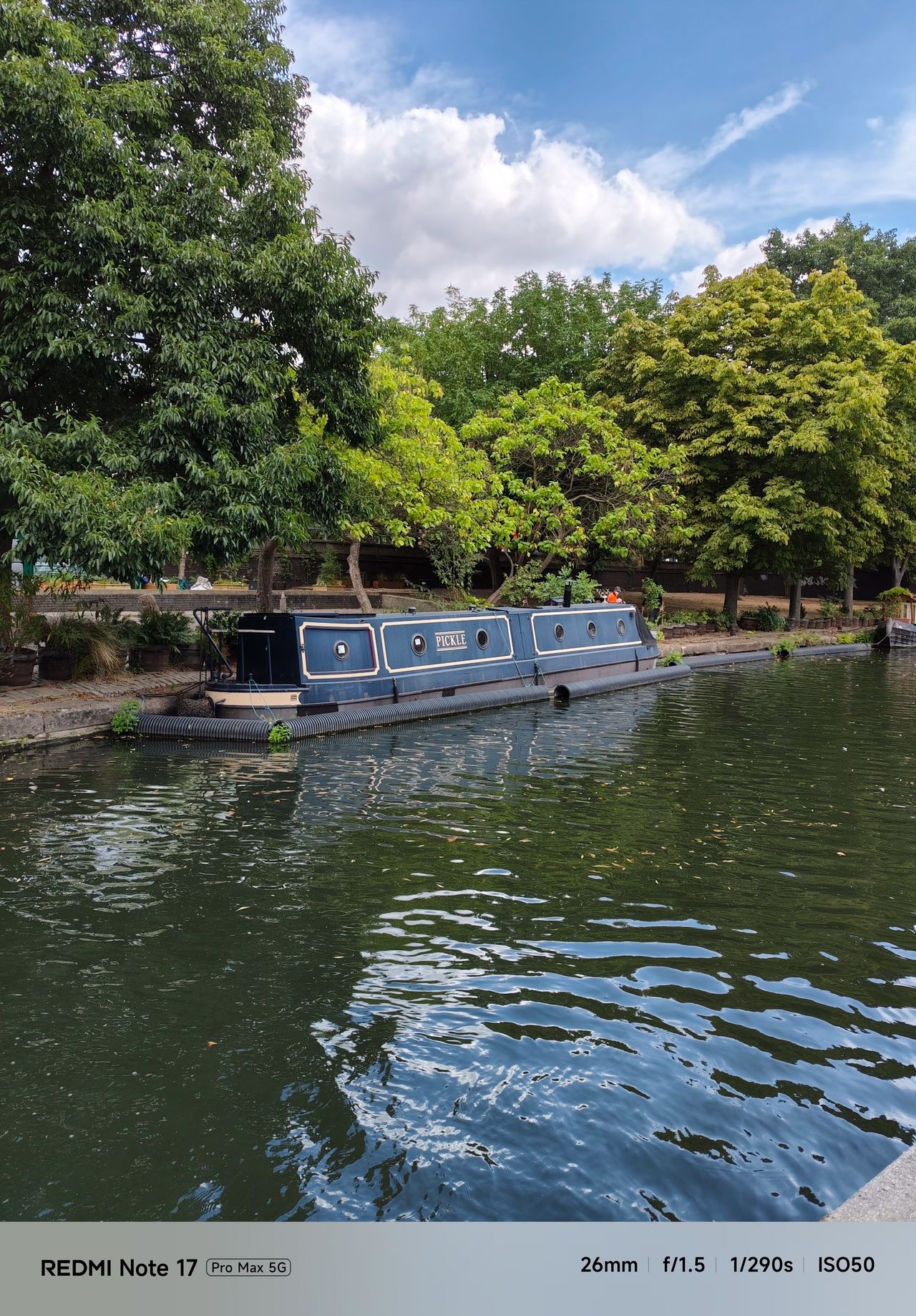 Blue narrowboat named Pickle moored beside leafy trees on a London canal.