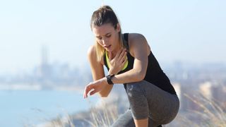 Woman with fitness tracker stopping during a sunny run, looking distressed