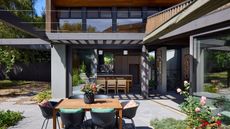 A backyard with stone flooring. There is also a dining table with chairs outside the home