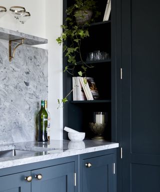 Gray-blue marble counters and tall back splash with matching shelving on gold brackets, with dark matte blue cabinet doors