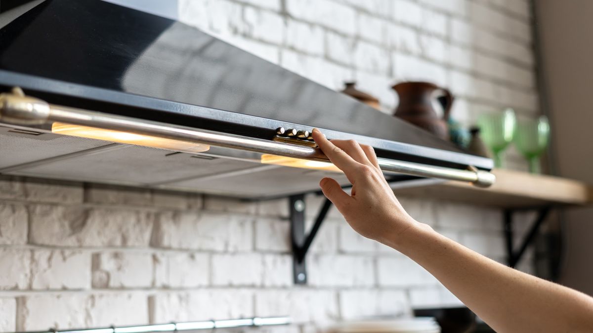 An unseen person presses a control button on a pyramid-shaped cooker hood. 