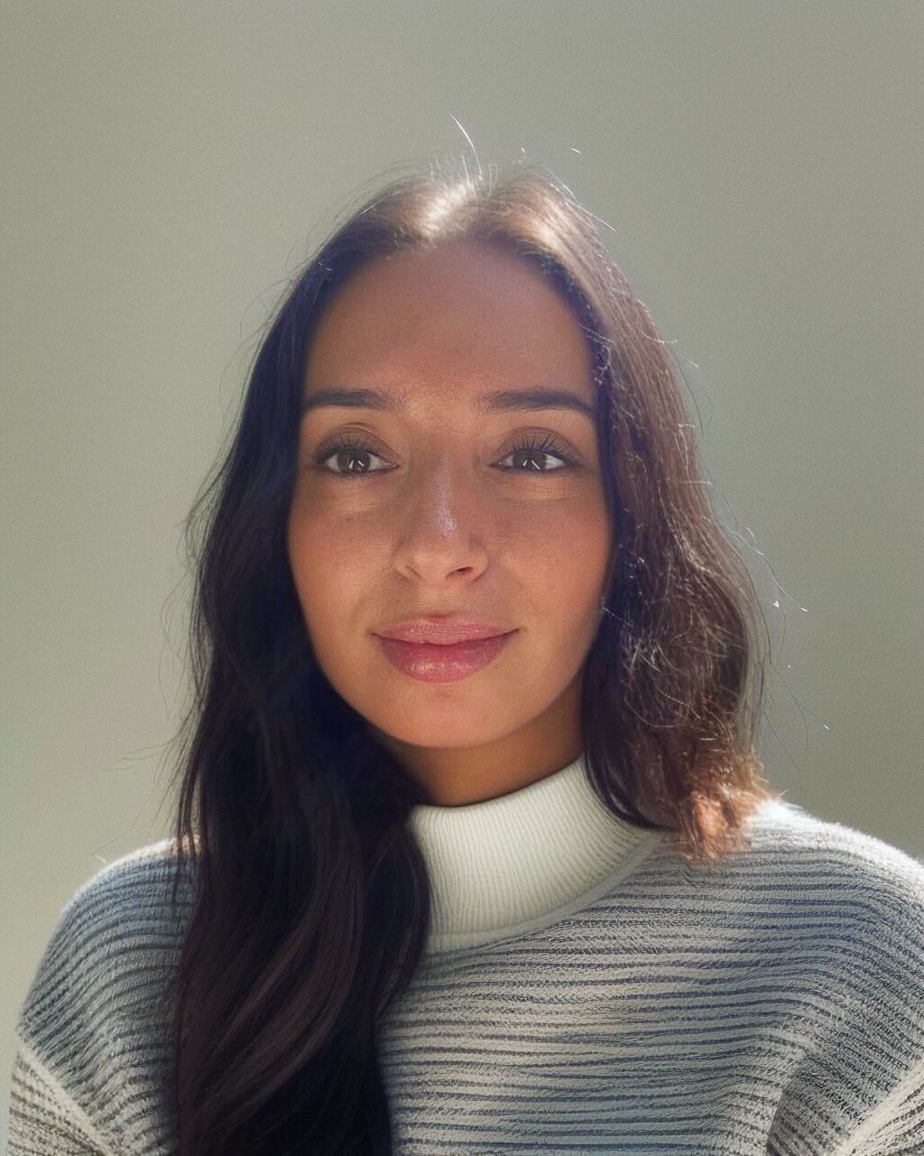 Susan Reis us a brunette lady wit long haur, she is pictured on a neutral background smiling at the camera