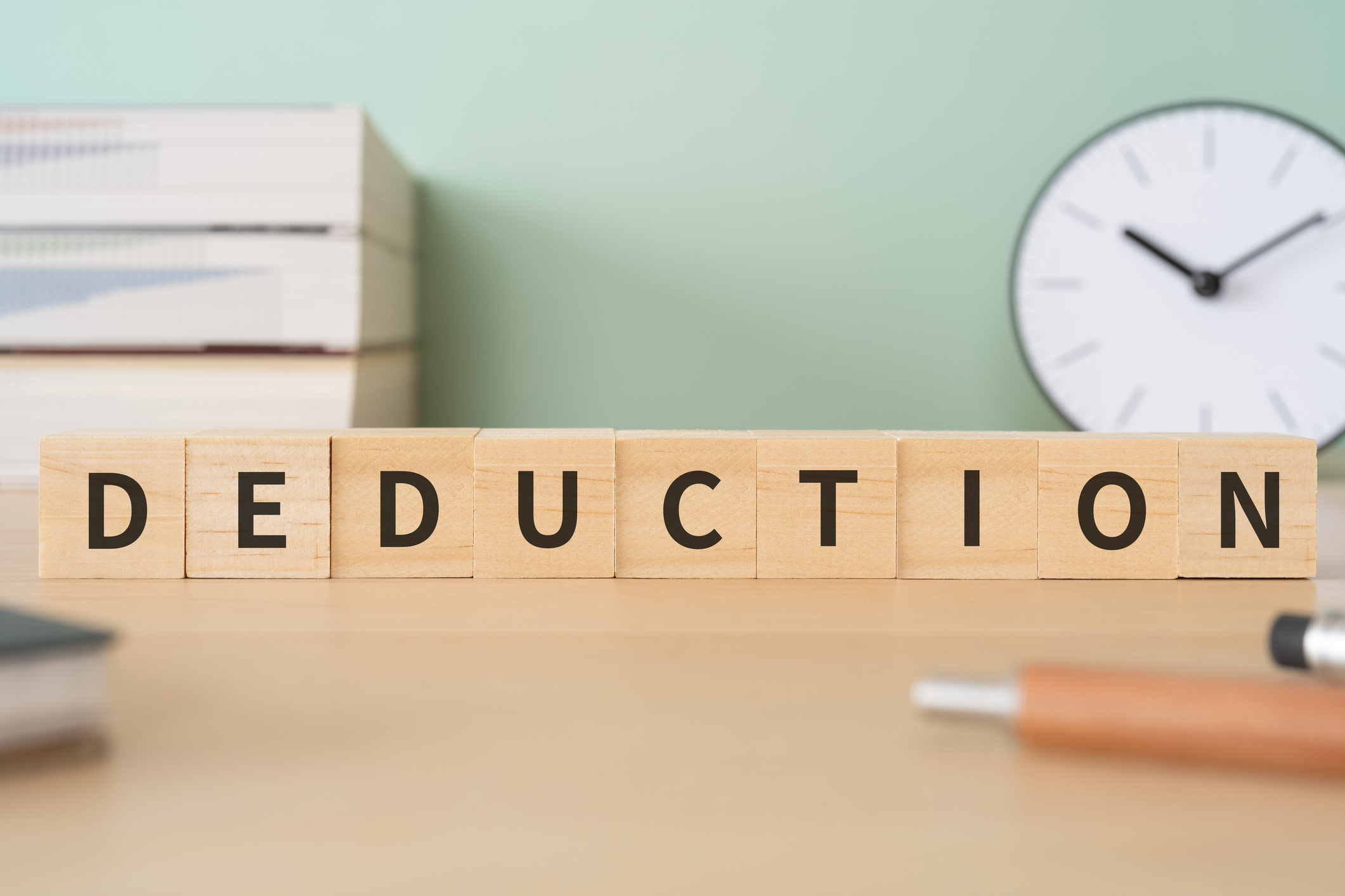 Wooden blocks with text that says "Deduction" on a desk with pens, books, and a clock.