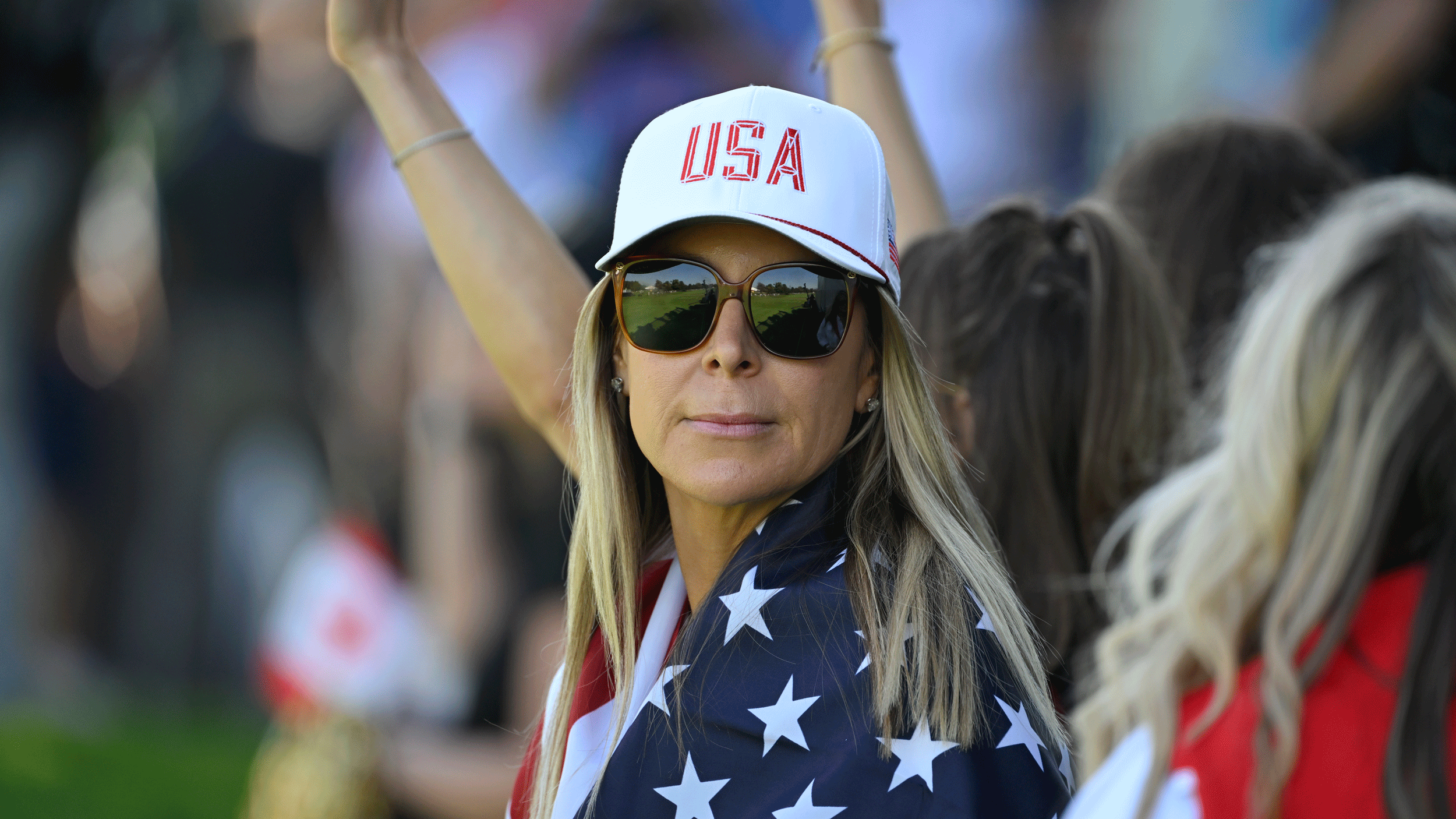 Brandt Snedeker's wife Mandy looks on through sunglasses at the 2024 Presidents Cup while wearing a Team USA cap and with a a US flag wrapped around her
