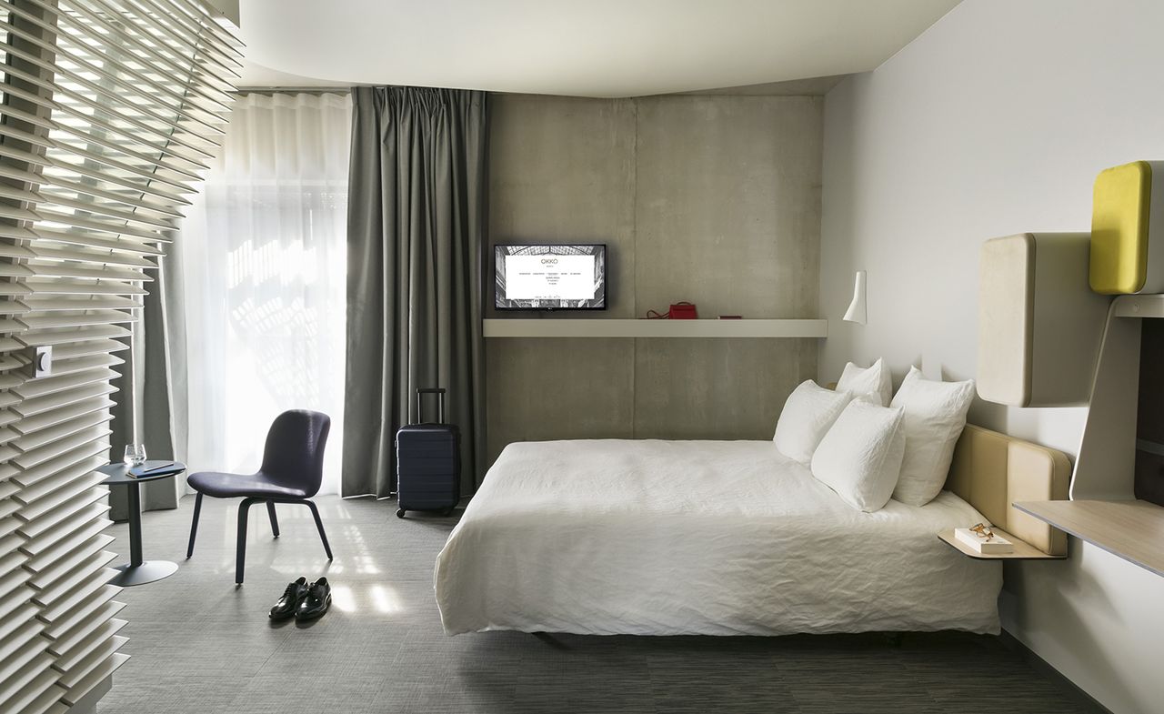 Bedroom in pale, neutral tones, with a chair and table, suitcase and shoes