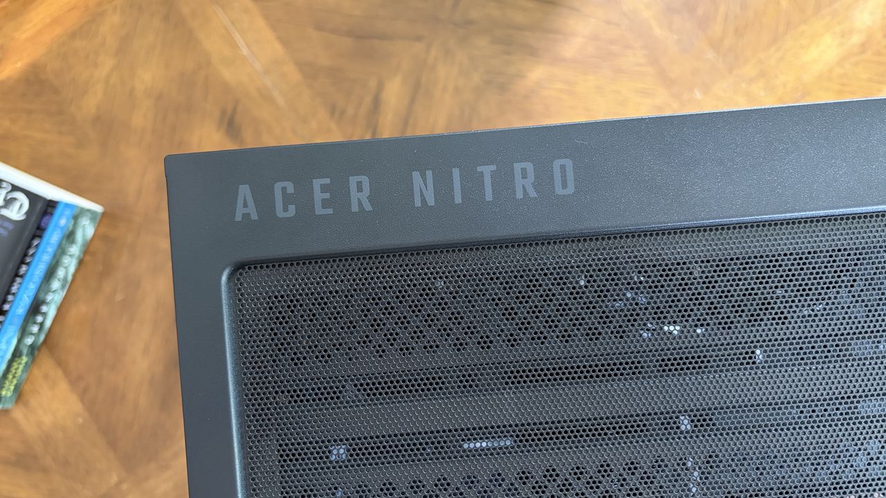 Top view of a black computer chassis labeled "ACER NITRO," featuring a mesh vent panel and set on a wooden surface.