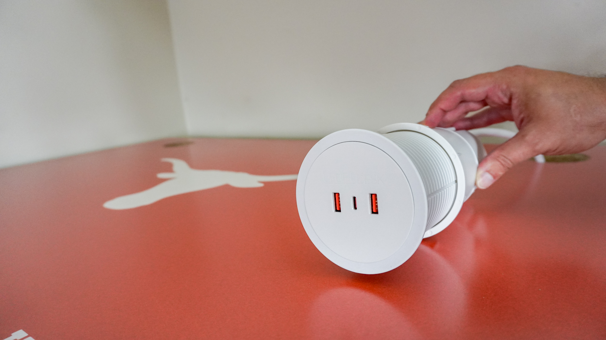 A person installing a power grommet at the back of a desk from the Uplift Desk Collegiate Collection