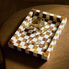 Brown and white checked tray with a watch and necklace inside
