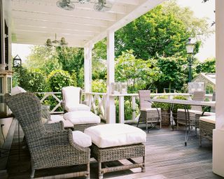 A white, wooden decked porch with wicker furniture and plants as garden privacy ideas.