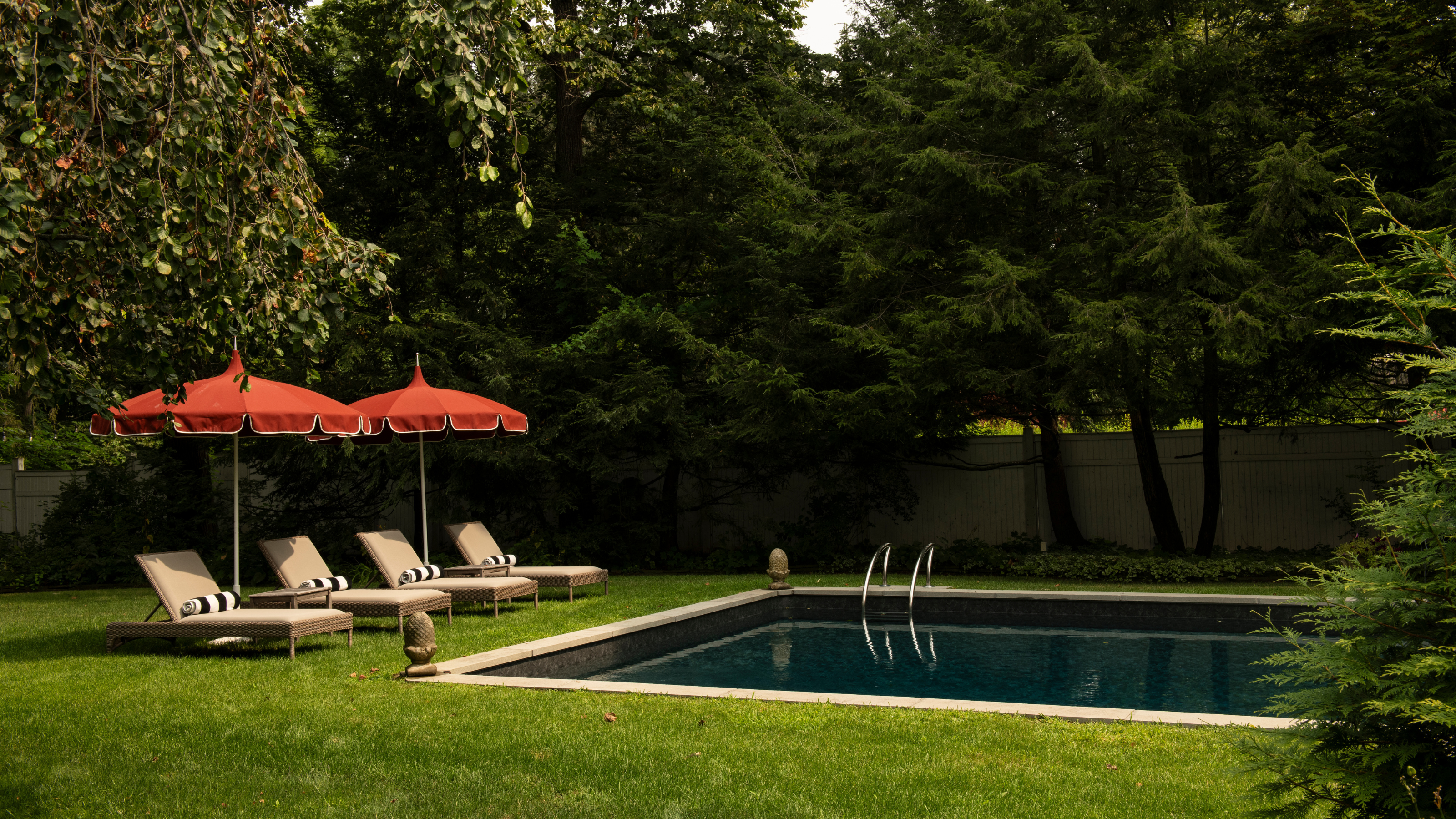 Serene backyard pool area featuring four chaise lounges and two umbrellas