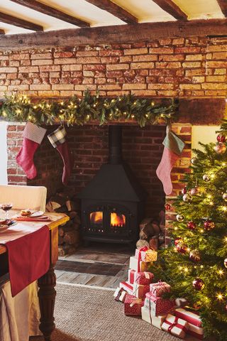 Christmas tree and inglenook with stove lit and stockings and garland and beams above