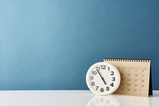 A clock and a calendar resting against a blue wall background