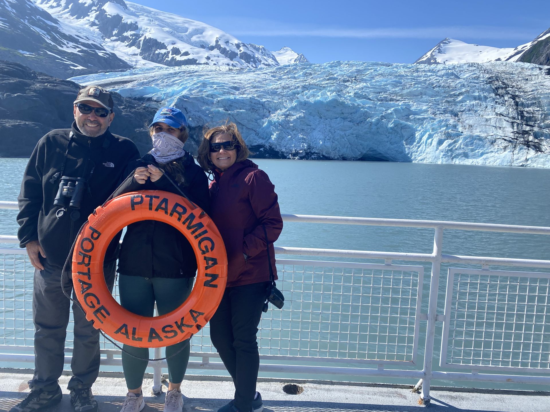 Parents and their adult daughter stand on a boat in front of a glacier in Alaska.