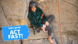 A female rock climber on a ledge smiling while wearing a green The North Face Osito Jacket