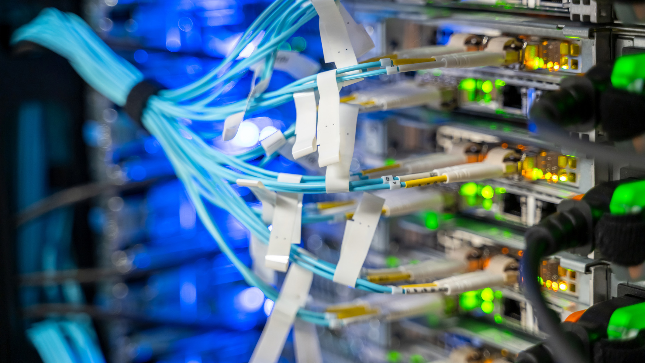 A close-up shot of networking routers and switches connected by neatly arranged fiber optic, twisted pair, and power cables within a data center.