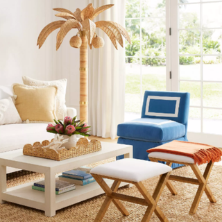 A living room with a white couch, a blue chair and two rattan and white stools