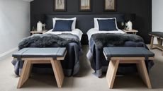 Bedroom with twin beds below a sloping ceiling, dark blue feature wall, grey carpet and walls. Converted farm buildings, a family home on a farm in the Cotswolds, home of George and Polly Phillips and their baby
