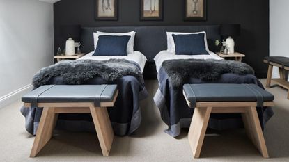 Bedroom with twin beds below a sloping ceiling, dark blue feature wall, grey carpet and walls. Converted farm buildings, a family home on a farm in the Cotswolds, home of George and Polly Phillips and their baby