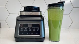 The Ninja 3-in-1 Food Processor with Auto-IQ BN800UK next to a to-go cup full of smoothie that was created in the appliance