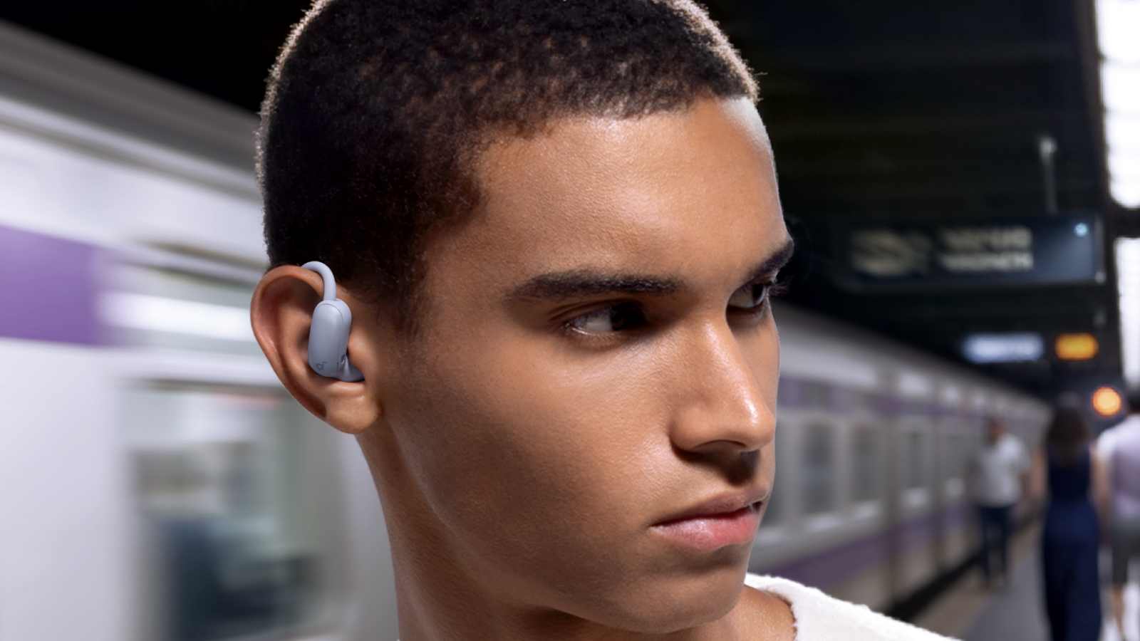 The Anker Soundcore Aerofit 2 Pro in a man's ear while he looks the wrong way to wait for the train.